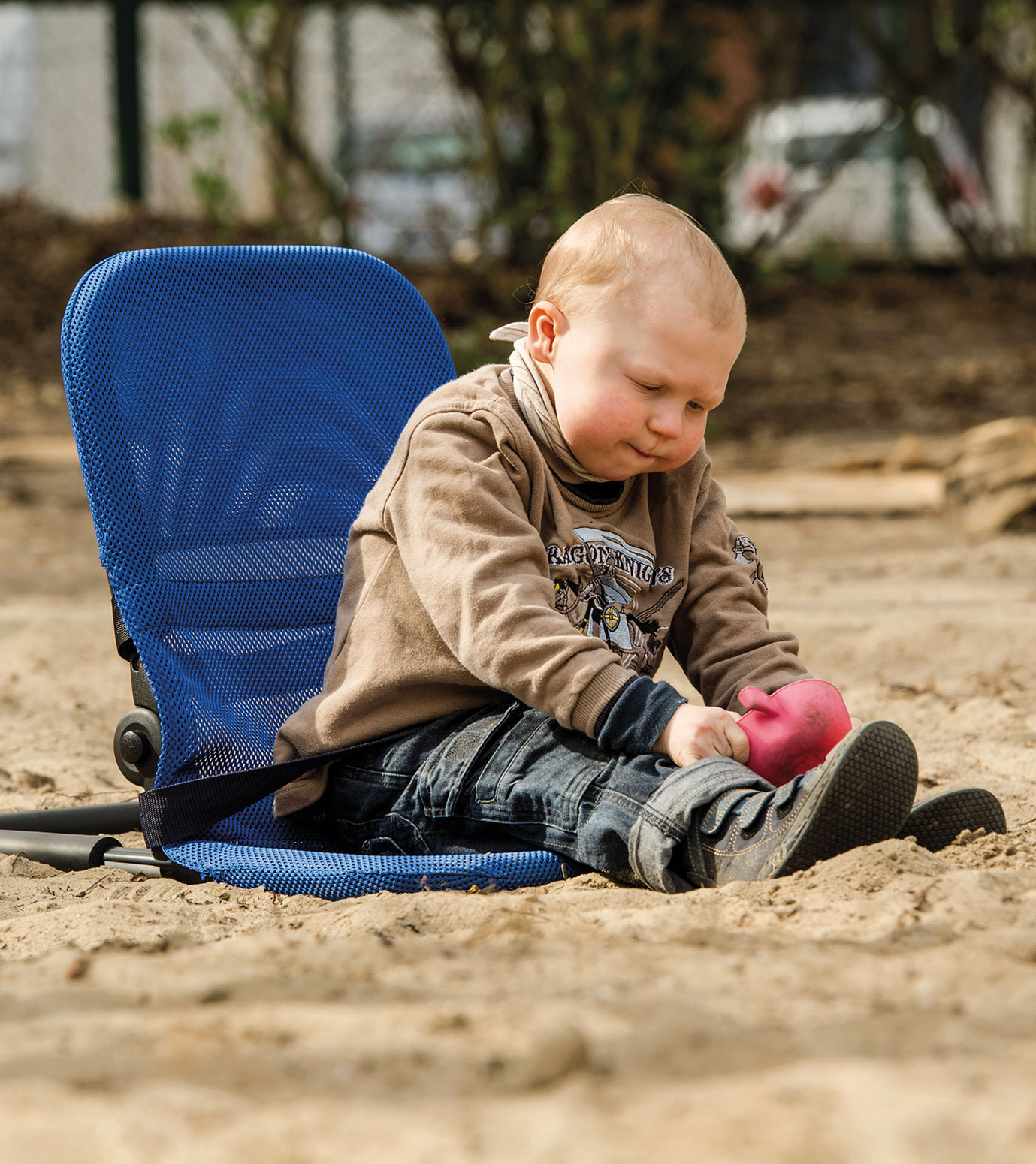Child with a disability plays in the sandpit in a mobile bathing seat